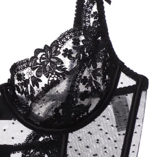 Close-up of the Amore Unlined Lace Bustier Bra Set by Petite Cherry. The lace features intricate floral patterns and delicate mesh detailing, creating a semi-transparent and elegant look. The edge of the bralette is adorned with scalloped lace trim.